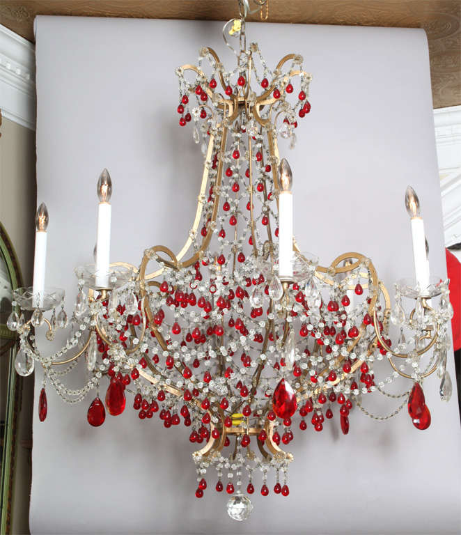 Magnificent chandelier, having eight gilded iron candlearms with etched glass scalloped bobeches, the entire fixture draped with strands of clear cut-crystal beads and accented by red teardrops and  clear prisms; finished by a faceted ball drop.