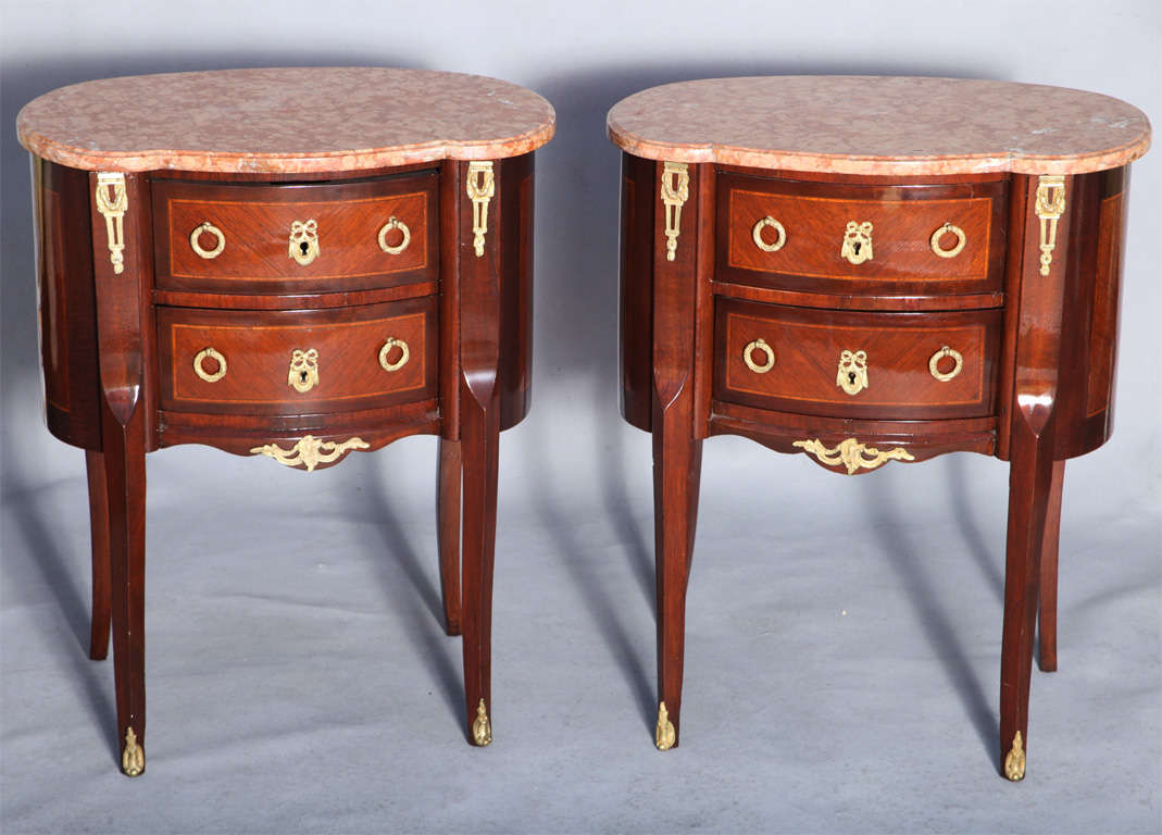 Pair of commodes, in transitional Louis XVI style, each having a ovalesque top of marble, on conforming base of mahogany veneers, sides and double-stacked drawers inlaid in chevron pattern with banding, bronze doré mounts pulls and escutcheons