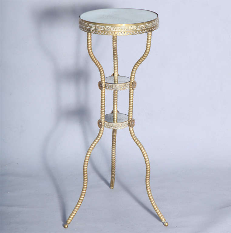 Three tiered Victorian repoussé and metalwork candlestand, having round top and shelves of distressed mirror, each surrounded by finely chased gilt brass, bowed and splayed round reeded legs affixed by rosettes at each shelf.