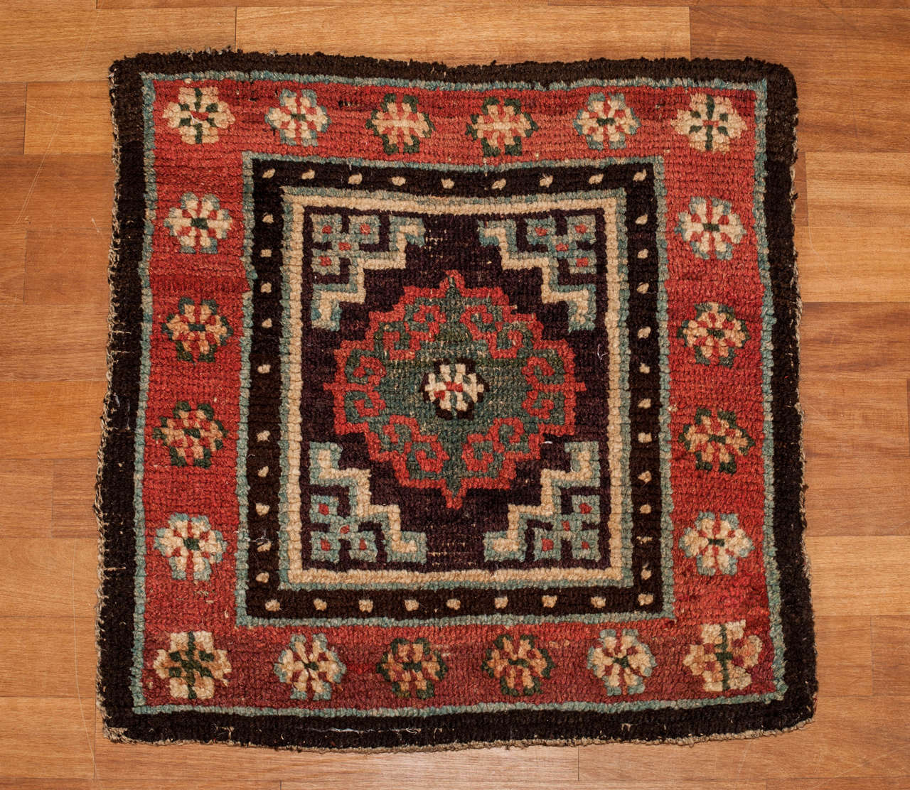 A beautiful and early example of meditation mat, ornated by a centralized green hooked motif with a red profile on a dark aubergine background, with stylized cloud bands on the four corners. Examples of this vintage are very hard to come by
