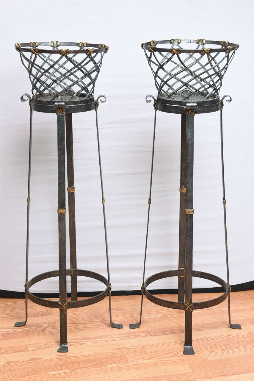 Striking pair of iron basket weave planters on stands with brass trim.