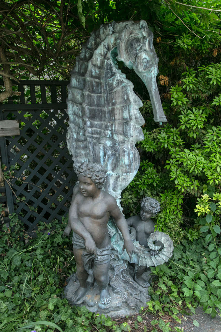 This large fountain, in the  form of a seahorse has three putti at its base, with the rear putto pointing outward.
The putti sit on a base of wave forms. Weathered green patina. We do not know if the tubing does create the fountain effect, but the