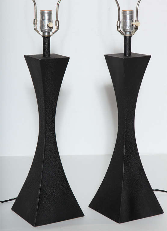 Signed pair of Mutual Sunset Lamp Company black enameled cast aluminum table lamps, 1950s. In the manner of Stewart Ross James. Featuring a double splayed form in Black painted metal. Heavy. Sculptural. Architectural. Modernist. Statement lighting.