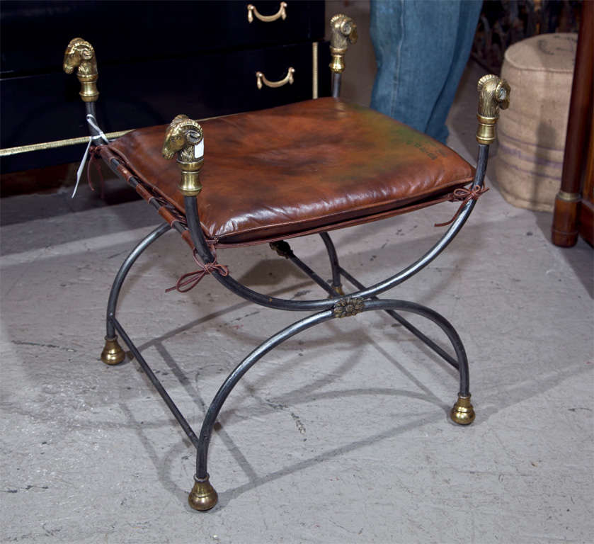 A charming French Directoire style metal bench, circa 1940s, decorated with bronze rams' heads, cushioned leather seat.
