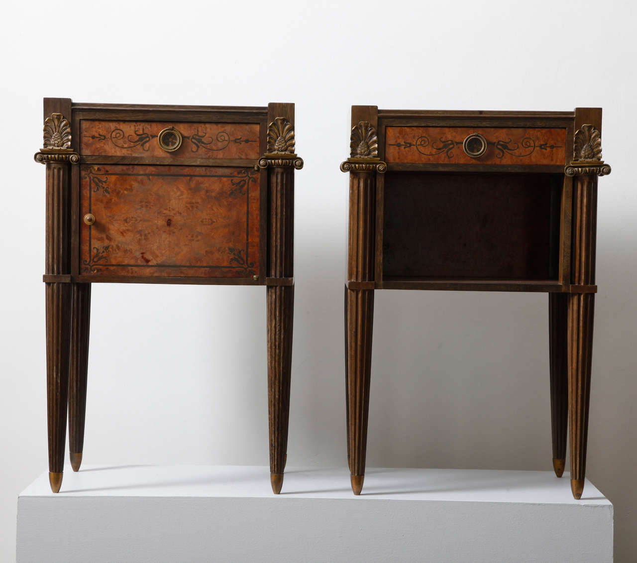 Pair of night tables in Neoclassical Art Deco style. They both have under the marble top a central drawer in burl wood decorated with floral and foliate neoclassical style marquetry, a gilt bronze circular handle in the middle and a gilt bronze