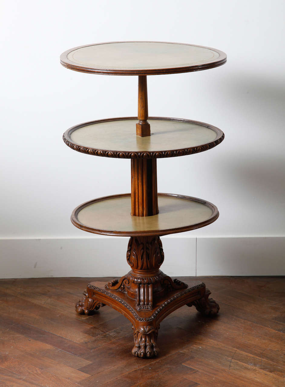 The three circular tiers are covered with green leather and have a moulded edge supported by a central column. The richly sculpted tripod base ends in lion paw feet and rests on brass castors.

H. 98 cm, Dia. of the trays 55 cm.