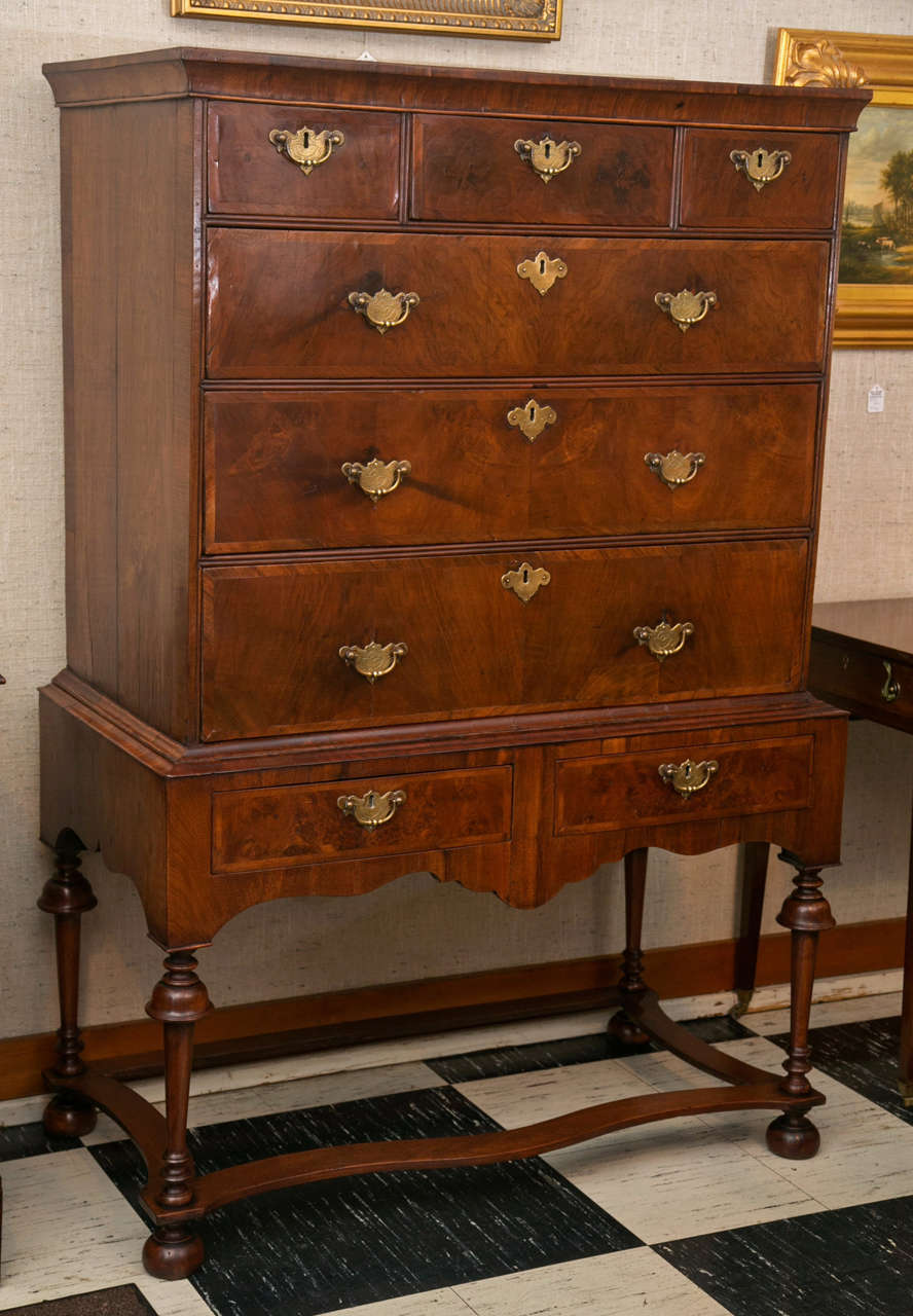 Taller than a chest of drawers and shorter than a highboy, this chest on stand more than measures up to task of storing things. A warm, brown walnut covers the front and sides while cross banding dresses the drawers adorned with brass bails with