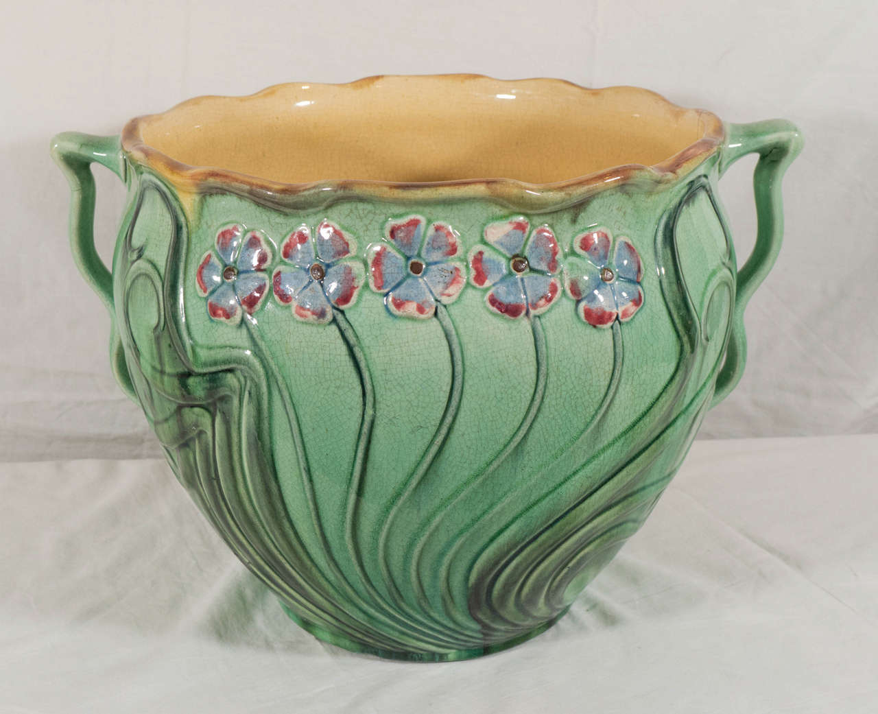 A large majolica jardiniere with an Art Nouveau floral design inspired by the flowing lines of flowers and plants. Both sides of the planter are decorated with a row of red and blue flowers on curving stalks. This planter will be perfect for orchids.