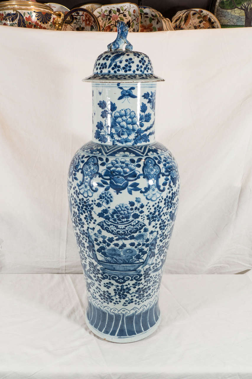 A tall pair of 19th century Qing Dynasty blue and white covered vases painted in underglaze cobalt. Decorated with an image of a large vase flanked by two attendants and a garden scene where butterflies and birds fly among sprays of flowering fruit
