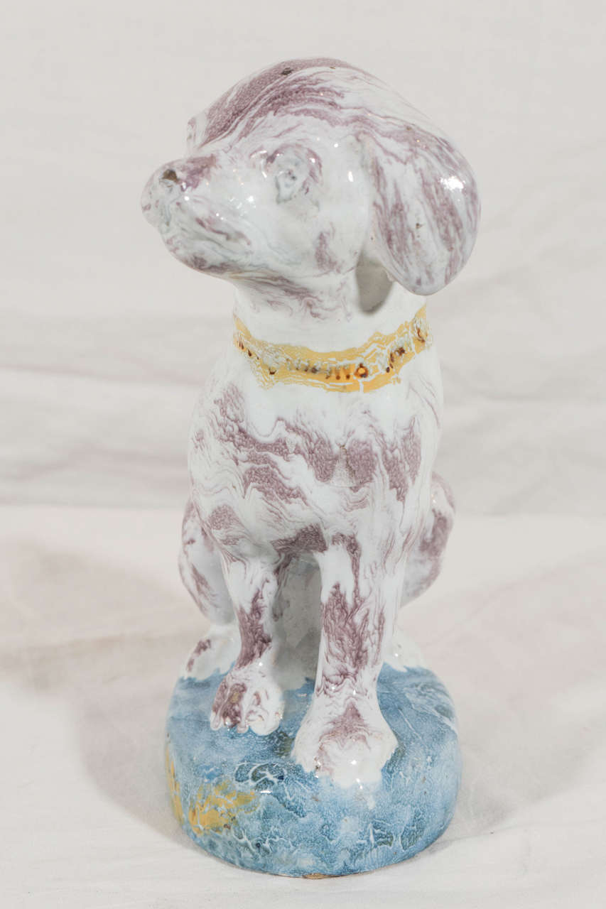 An 18th century Brussels Faience figure of a spaniel, naturalistically modeled, splashed in manganese he wears a yellow collar, and is seated on a blue oval base. This charming puppy will make a wonderful addition to any dog lover's home. Requiring