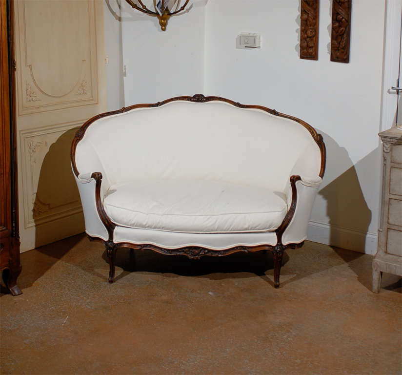 A French Louis XV style walnut settee from the 19th century with wraparound back, scalloped skirt, cabriole legs and new double welt upholstery. This French walnut canapé features an exquisite wraparound back adorned with a sinuous upper rail marked