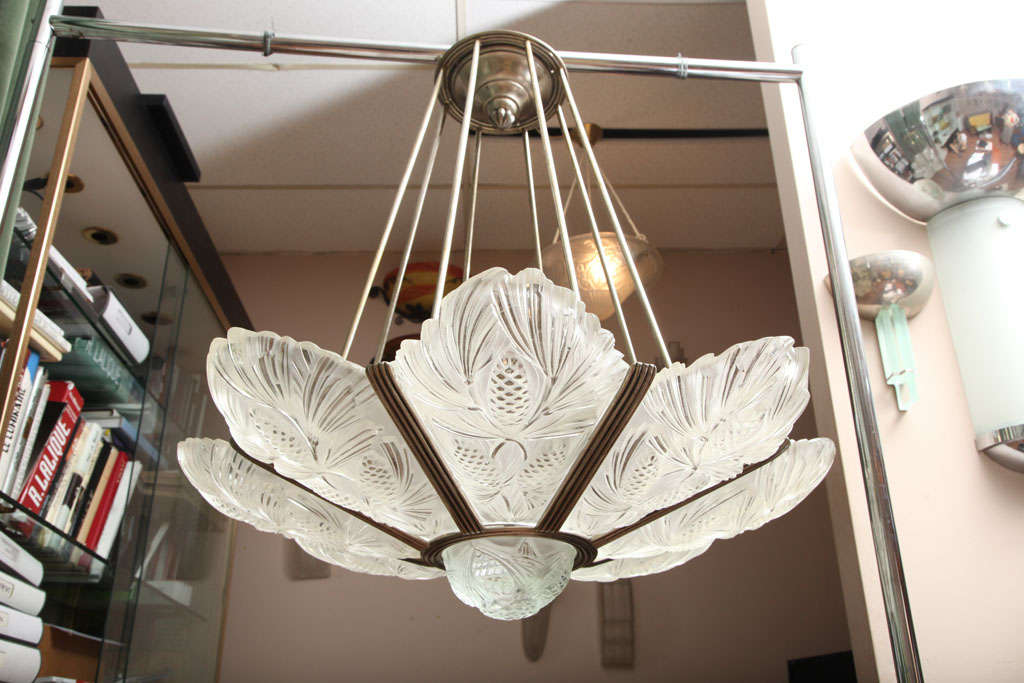 MARIUS ERNEST SABINO 
Art Deco Chandelier, c. 1925
Clear and frosted glass molded with pine cone motifs and mounted in a silvered bronze frame. 
Diameter : 86 cm. (33 7/8 in.) 
Each plaque signned SABINO PARIS DEPOSE 
Ref: Janneau “Le Luminaire