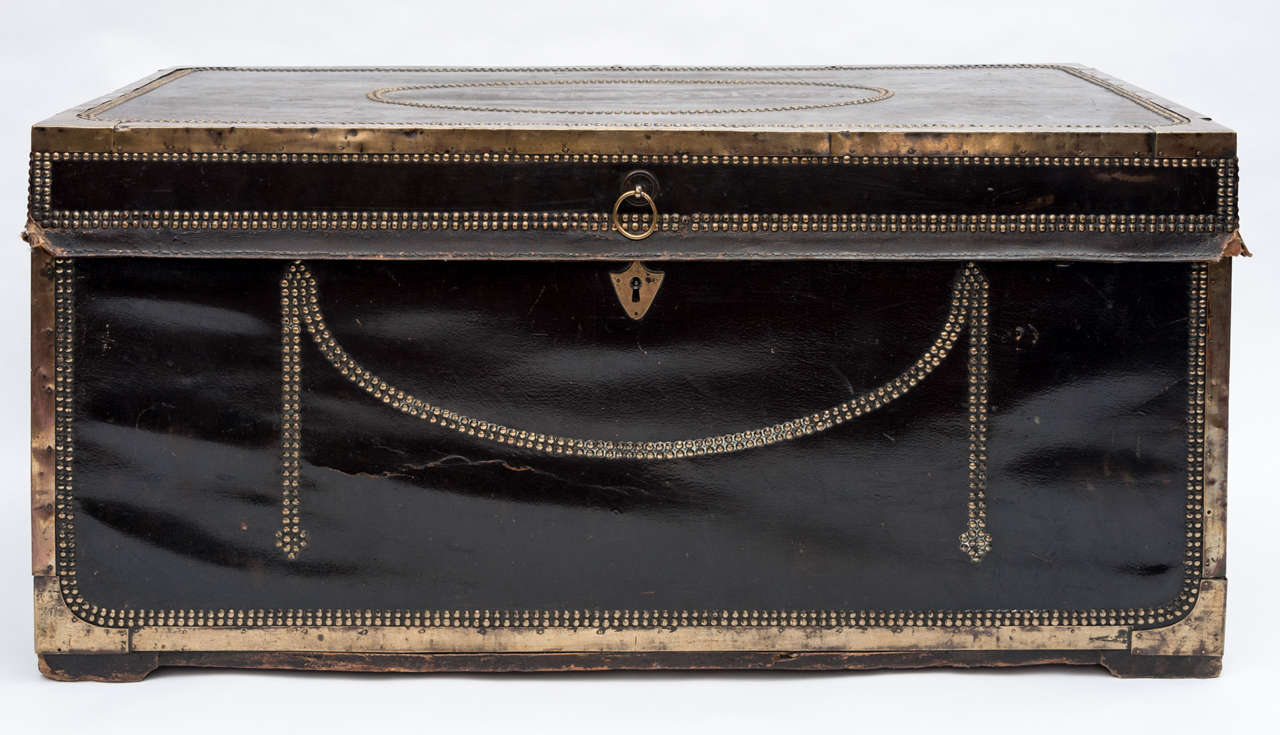 Early C19th black leather and brass bound camphor trunk, the lift up top with a brass bound edge and a brass studded oval panel with the name 'Captain J W Smyth.' The front with a brass studded swag, the sides retaining the original brass carrying