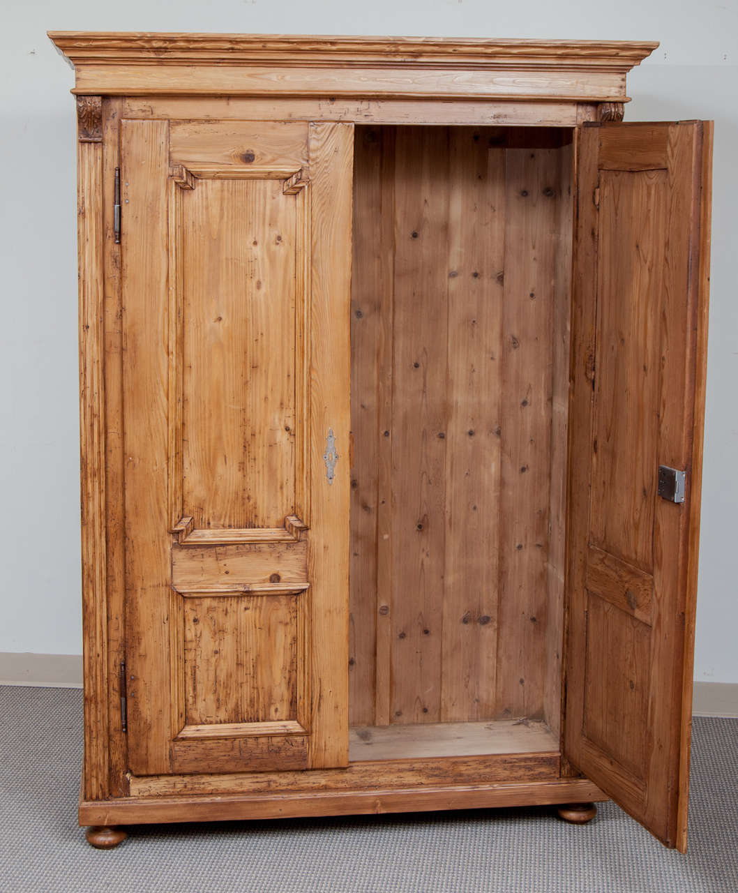 A handsome two door pine armoire featuring two panels to each door.  The doors, mounted on iron fiche hinges, are flanked and separated by applied fluting with bold acanthus leaf corbels.