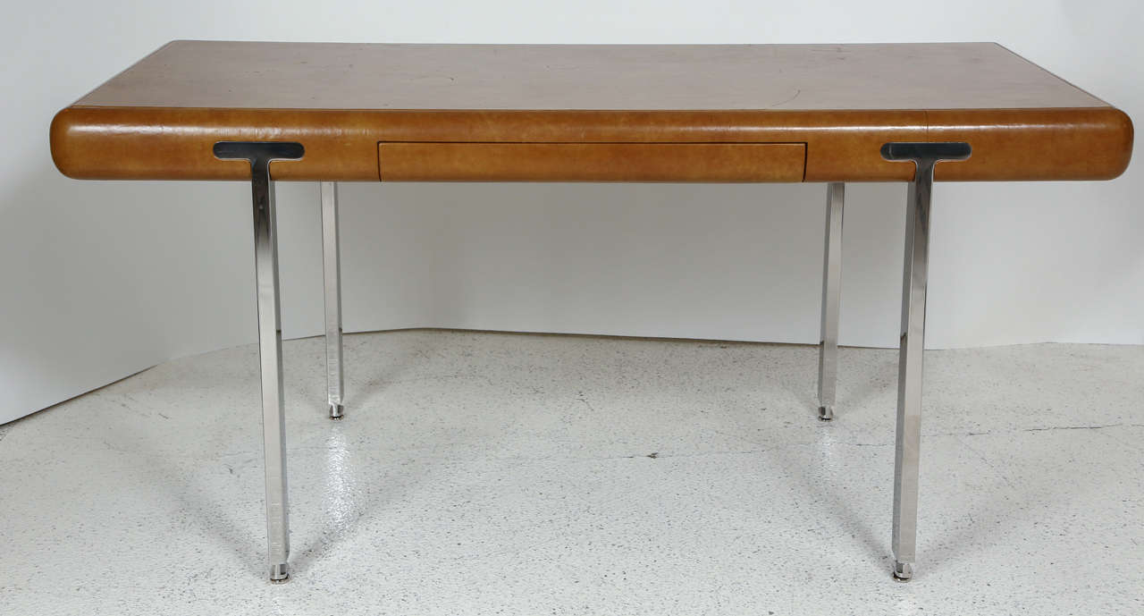 A handsome cognac leather topped desk with a single drawer and inset polished stainless steel legs. The legs have levelers at the bottom. The underside of the desk is marked with a Northrop Corporate control tag, so this desk was likely custom made