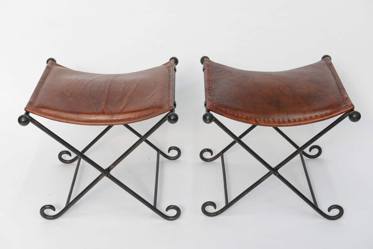 Beautiful in reddish-brown laced edge leather seats, this pair of 1940s wrought iron X-benches have an elegant simplicity and subtle Art Deco styling. In wonderful original condition, one bench more formed from sitting. The bases are collapsible