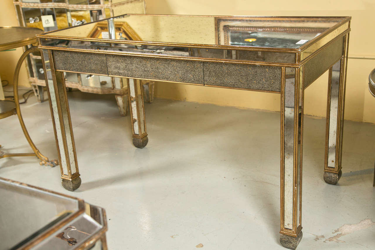 An attractive Mid-Century Modern style desk, gold painted frame veneered with mirror plates, the rectangular top over a narrow frieze fitted with two sliding drawers, raised on squared legs ending in toupee feet.