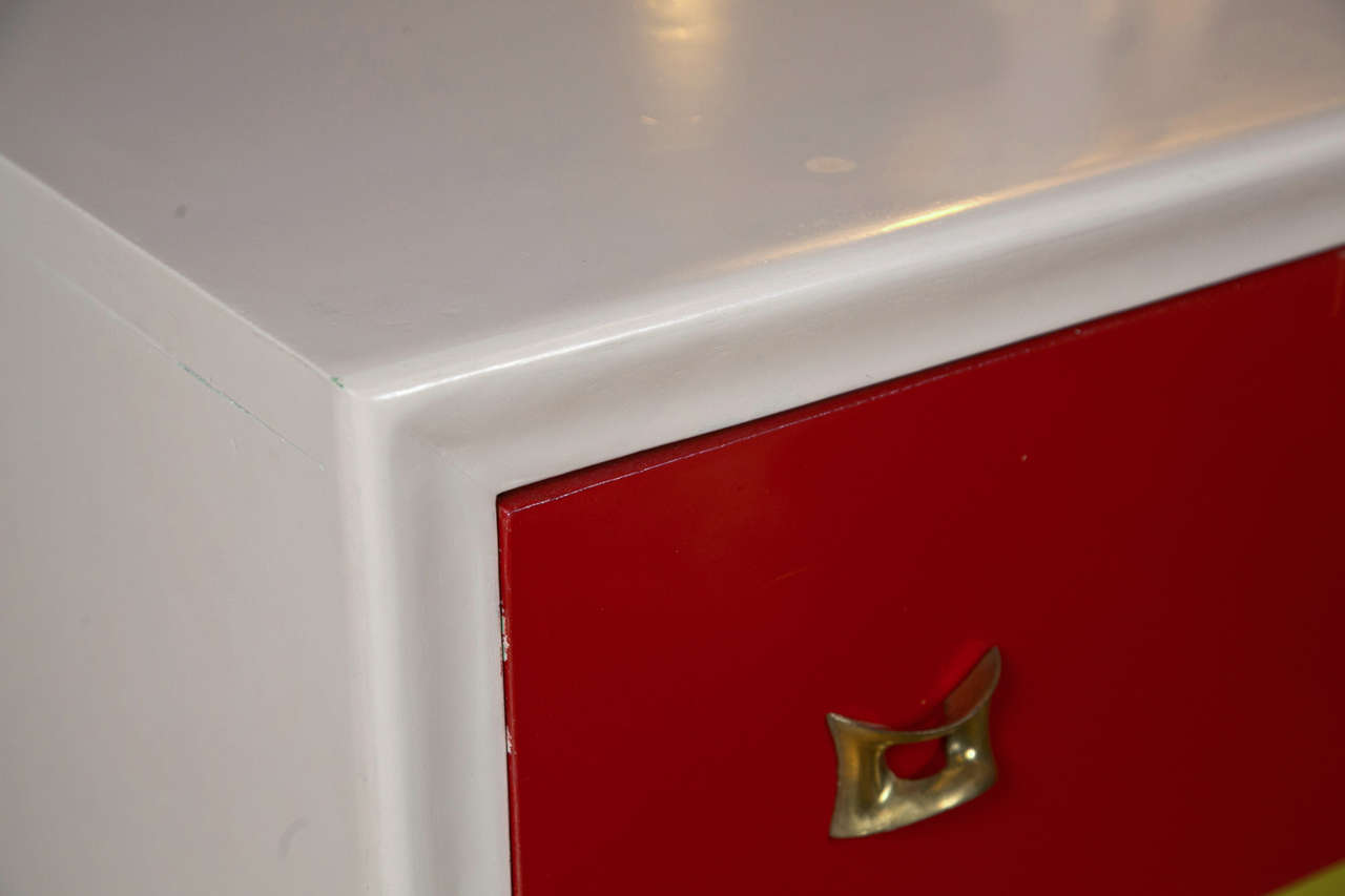 Pair of Mid-Century Modern style chests of drawers, each having the white painted enclosing case fitted with three drawers of red, green and blue color, raised on a plinth.
 