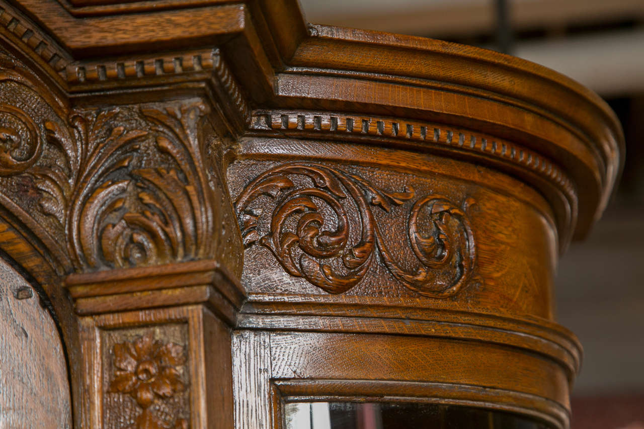 A finely carved china cabinet by Horner Brothers. This quarter sewn oak cabinet having square feet leading to a lower carved drawer flanked by winged miniature lions. The upper casing with glass shelves and a mirrored panel back. The Demi Lune glass