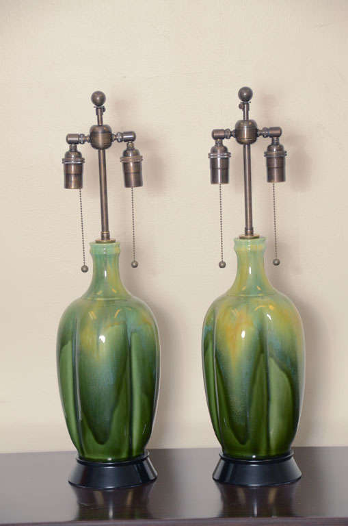 Pair of ceramic lamps produced by Haeger pottery, which have a wonderful drip glaze finish in varying tones of green. The lamps are mounted  on black gloss finished bases and are newly rewired with antique double clusters and silk rayon cords.