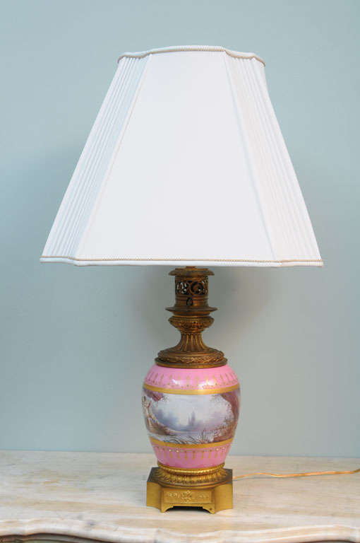 A pair of pink serves bronze mounted porcelain electrified oil lamps with painting of cupids, circa 1850.
