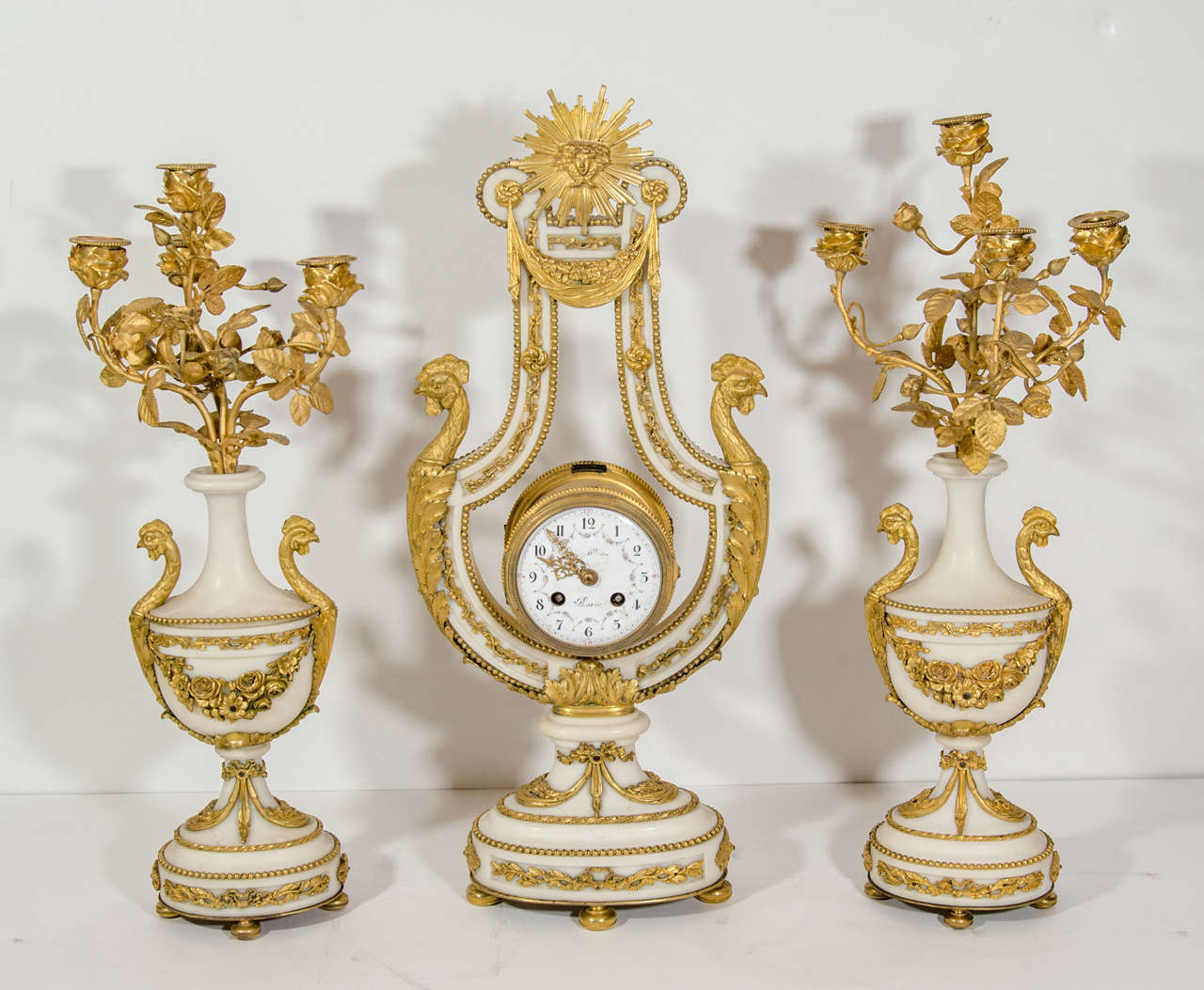 A Magnificent Antique French Louis XVI Style hand carved white marble and gilt bronze three piece Lyre form clock set of exquisite craftsmanship embellished with gilt bronze figural masks of roosters. This unique clock set consists of a very unusual