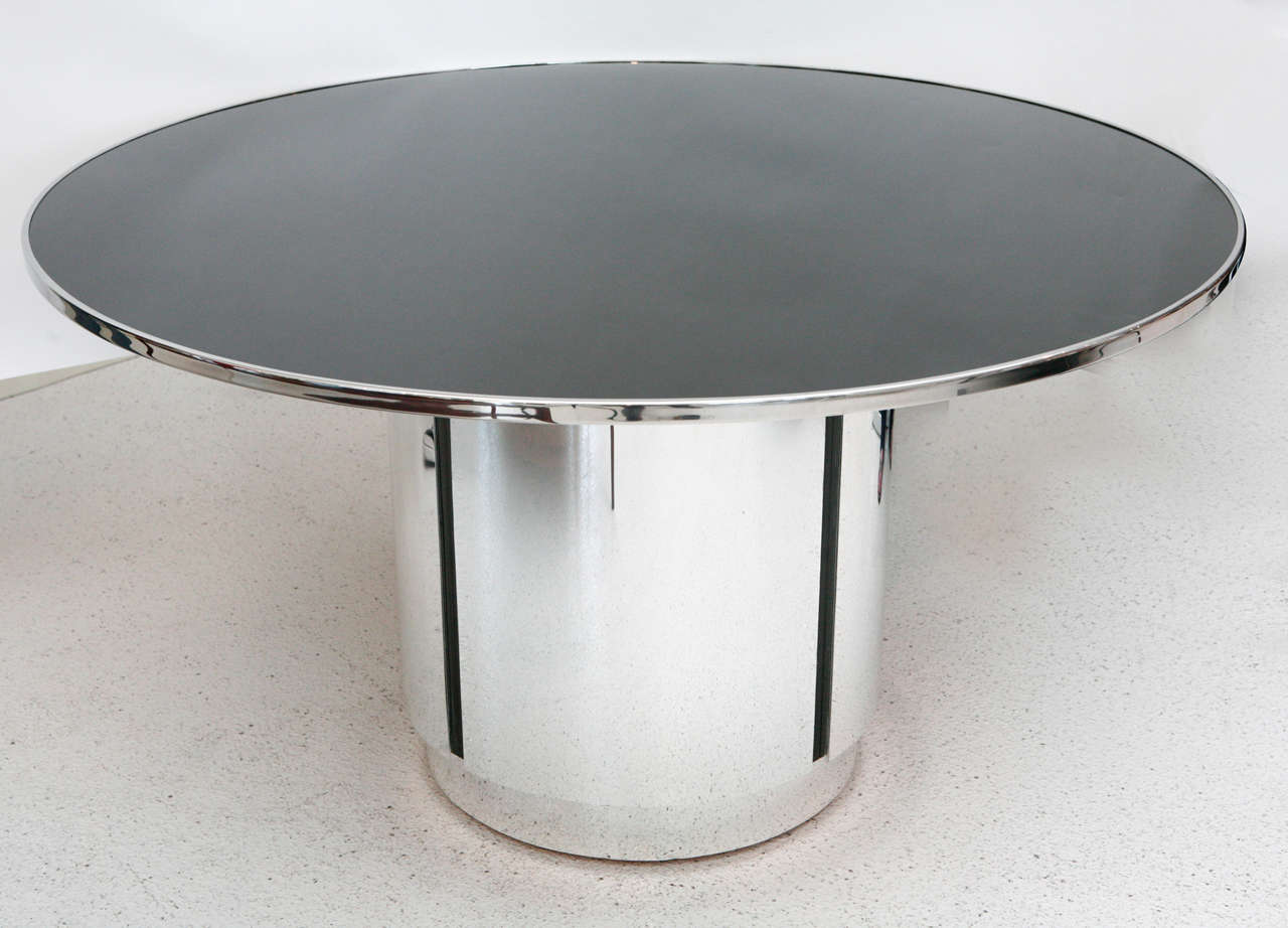 A glam round black glass and chrome pedestal base dining table with a recessed plinth. The base is accented with black channel details and the removable black glass top is banded in chrome.  Would also make a beautiful entry table.
