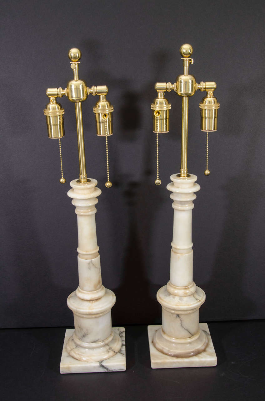 Pair of classical style carved alabaster two light column lamps on round plinths and square bases.
