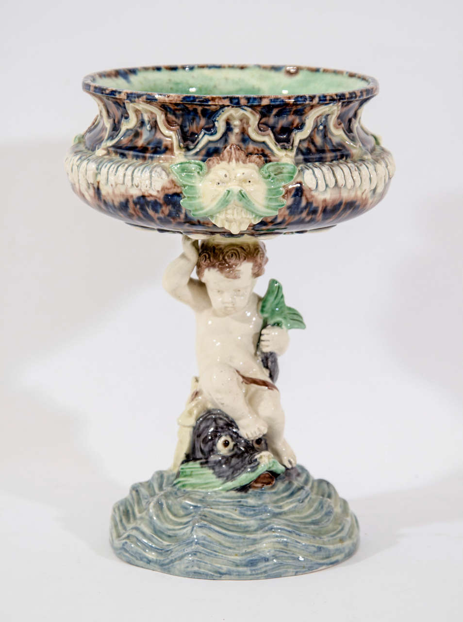 French Majolica Tazza on Cherub and Dolphin Pedestal in Green, Blue, and Cream Tones by Thomas Sergent.  France, c. 1880

8 inches diameter x 10 inches high
