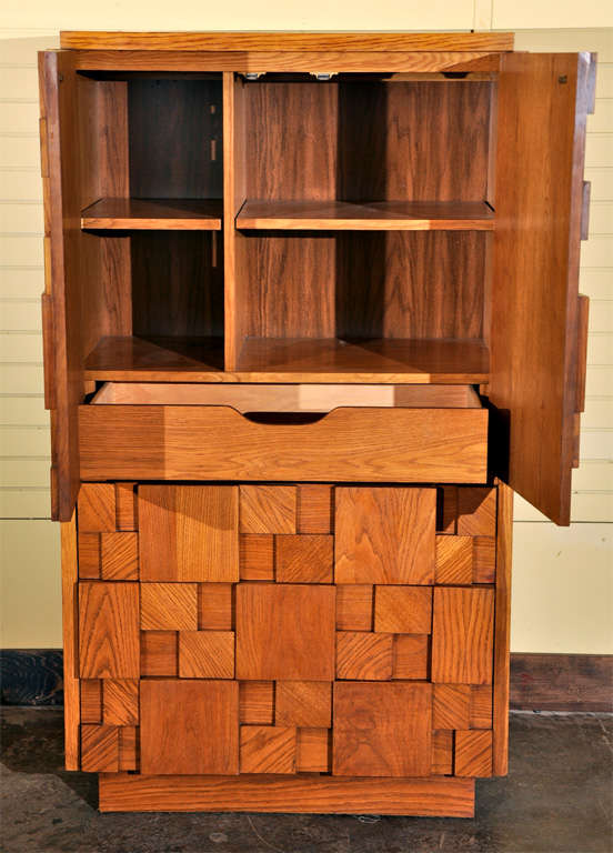 Manufactured by Lane, located in Virginia, the front of this oak dresser’s design is made up of superimposed wood panels ranging in different sizes. The upper half of the dresser opens up with two doors. A divider splits up a portion of the interior