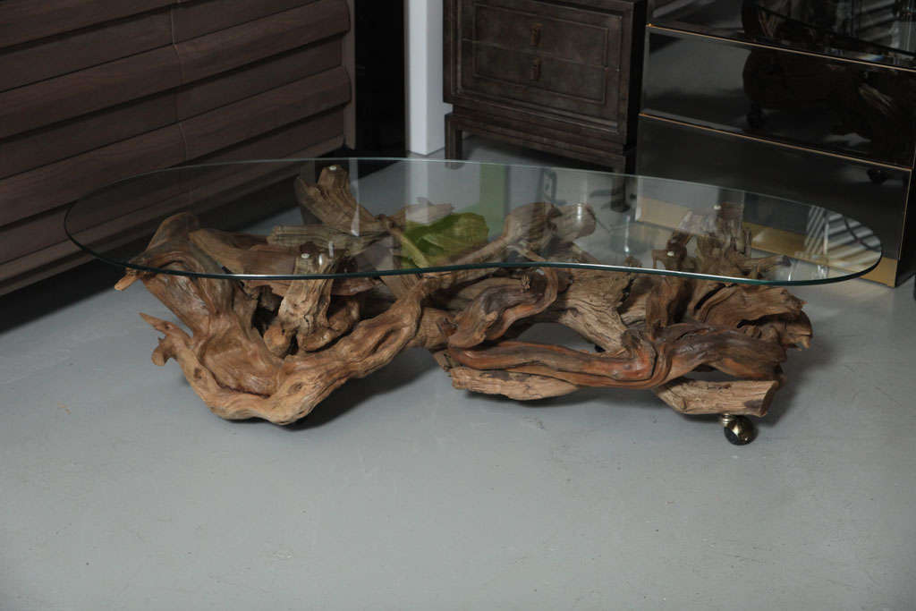 An Old Florida favorite, this 60's driftwood coffee table is crafted from poetically-pieced-together beach finds in their naturally weathered shades of taupe and brown. The kidney-shaped glass top follows the form of the organic (wheeled) base.