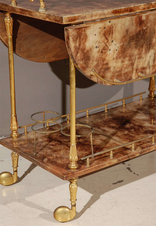 A goat skin/vellum drop leaf drinks trolley designed by Aldo Tura. The fittings and galleries are all fabricated out of polished brass and the secondary wood is mahogany. The wheel covers on this cart are are nicely detailed. The cart is 30
