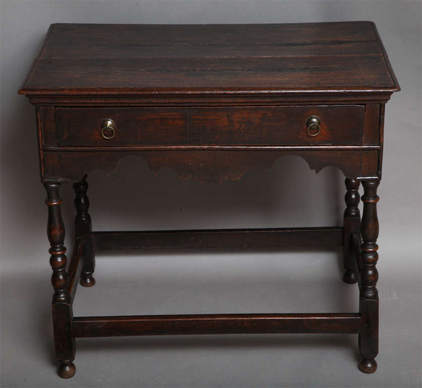 Fine William and Mary period English oak side table, the thumb molded top with ogee shaped under molding, the single drawer having line inlaid panels and half round molded facade, over heavily scalloped apron and standing on vase and ball turnings,