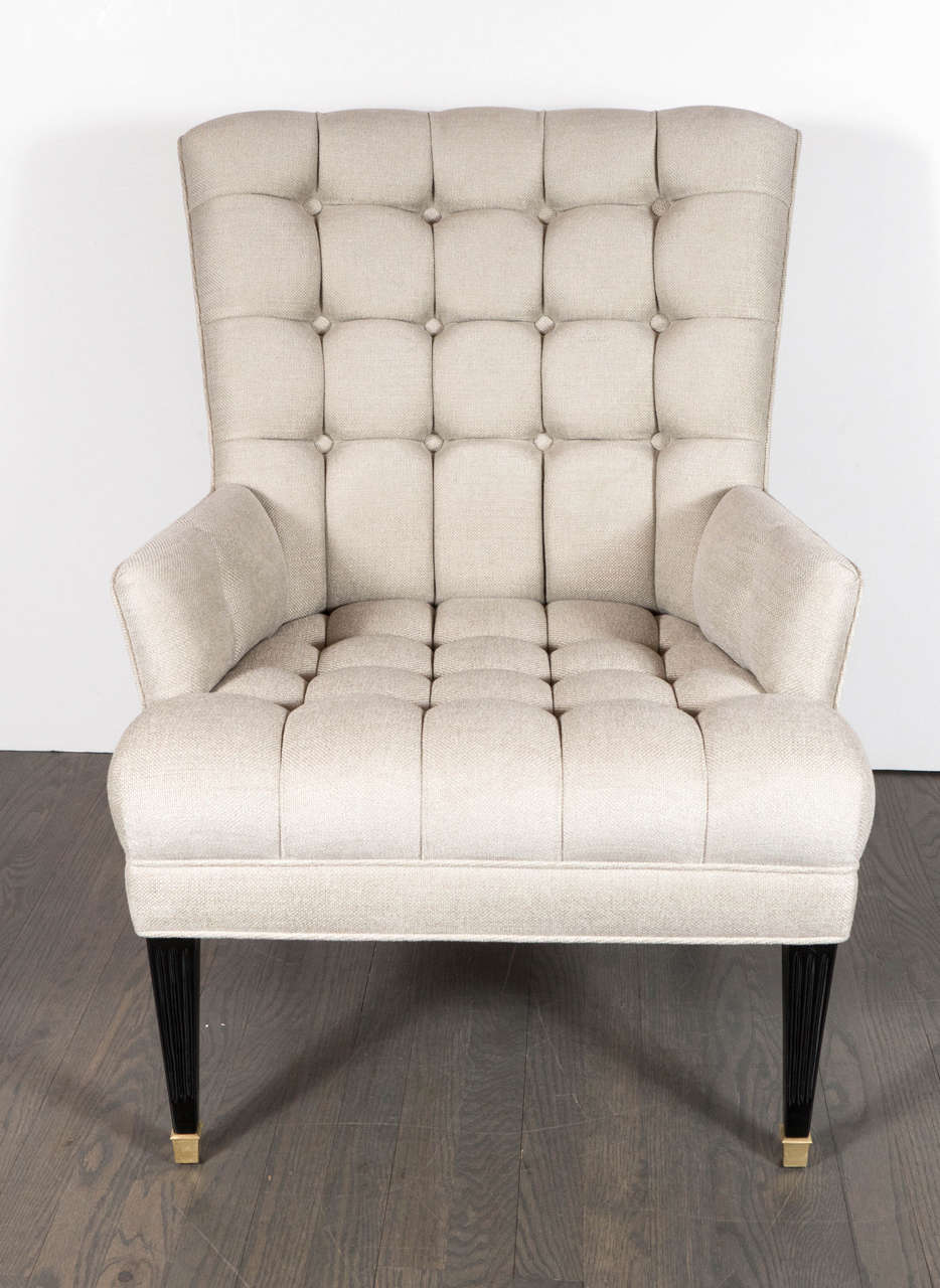 This handsome and refined Mid-Century Modern armchair- realized in the manner of William Haines- features a tapered high back and a tufted biscuit pattern seat and back in new oyster shell upholstery with rectangular saber style ebonized walnut legs