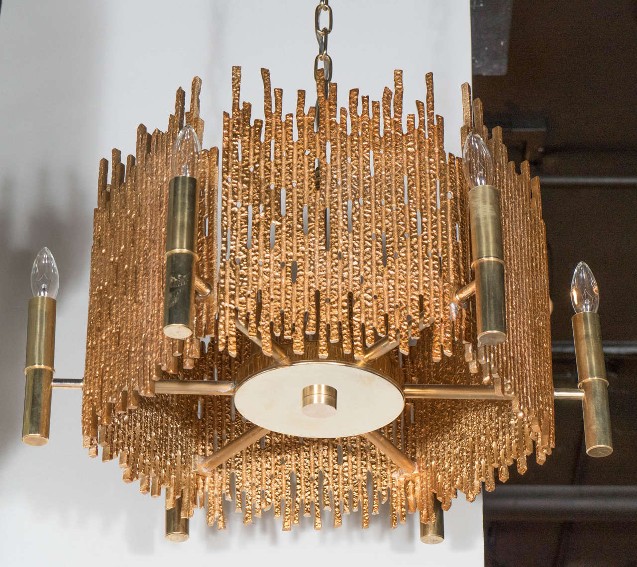 This very sophisticated chandelier features six Brutalist brass panels emanating out from a central stem. It is also fitted with six lights equipped to hold candelabra bulbs. This chandeliers height can be adjusted to suit. This has been completely