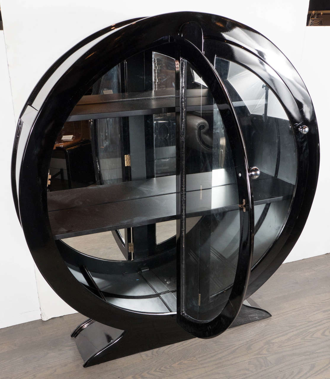 This streamlined design Art Deco cabinet features a circular highly stylized cabinet design on a plinth base in black lacquer . It also features two chrome machine age ball pulls and is also fitted with three shelves and a mirrored back. This piece