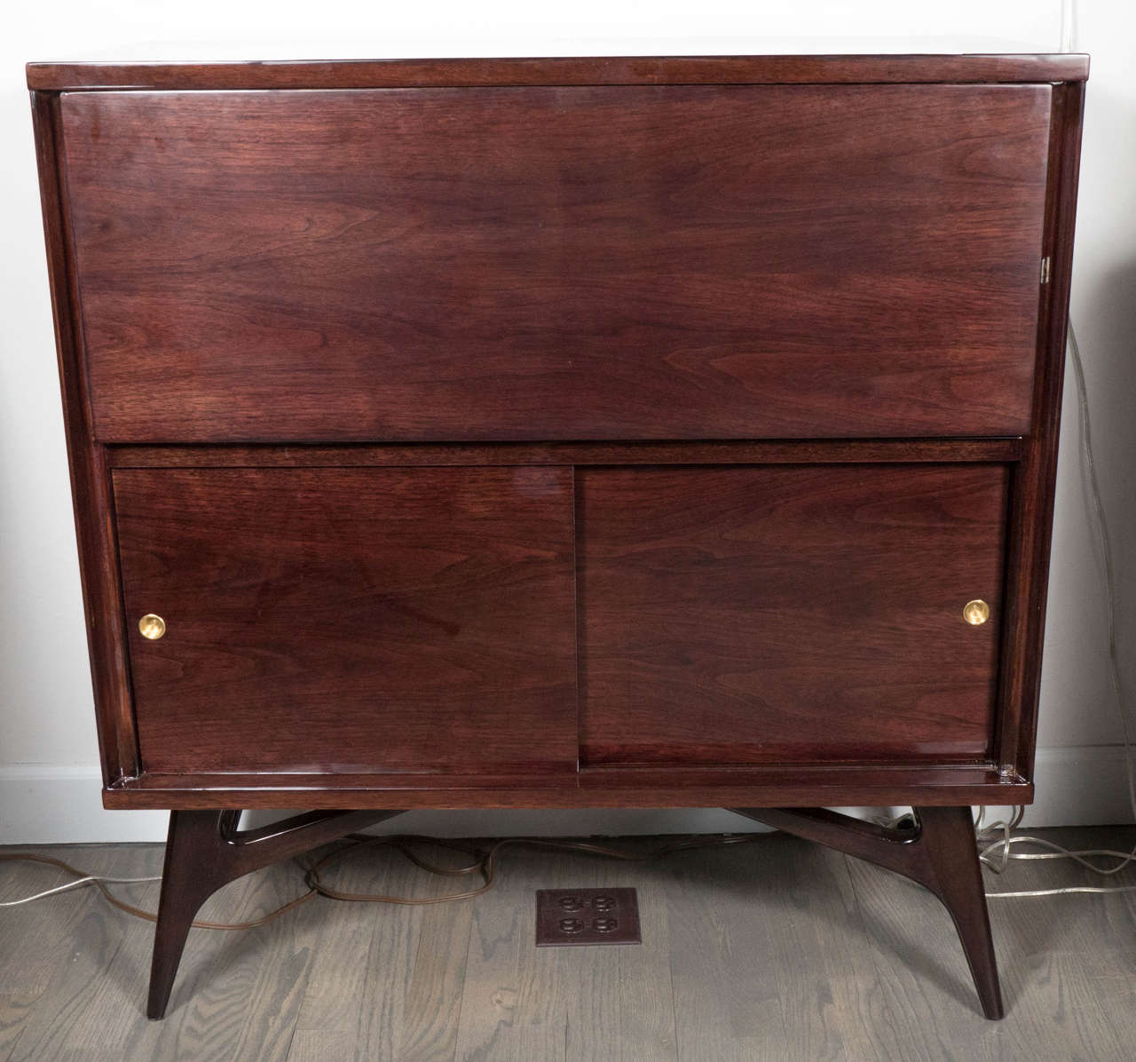 This refined Mid-Century Modernist bar cabinet was realized, circa 1950 in the United States. It was handcrafted from bookmatched walnut (that offers a particularly stunning grain) with brass details throughout. The top cabinet area employs a