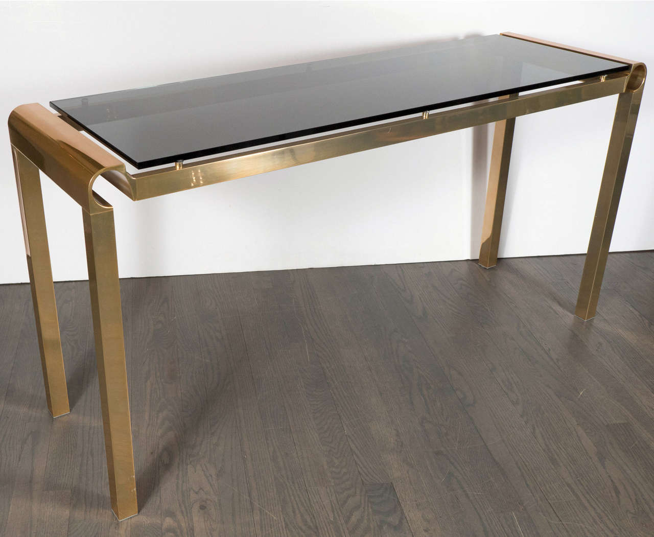 This superb Mid-Century Modernist console in the manner of Karl Springer features a floating smoked glass top with a stylized linear brass frame and detailing.