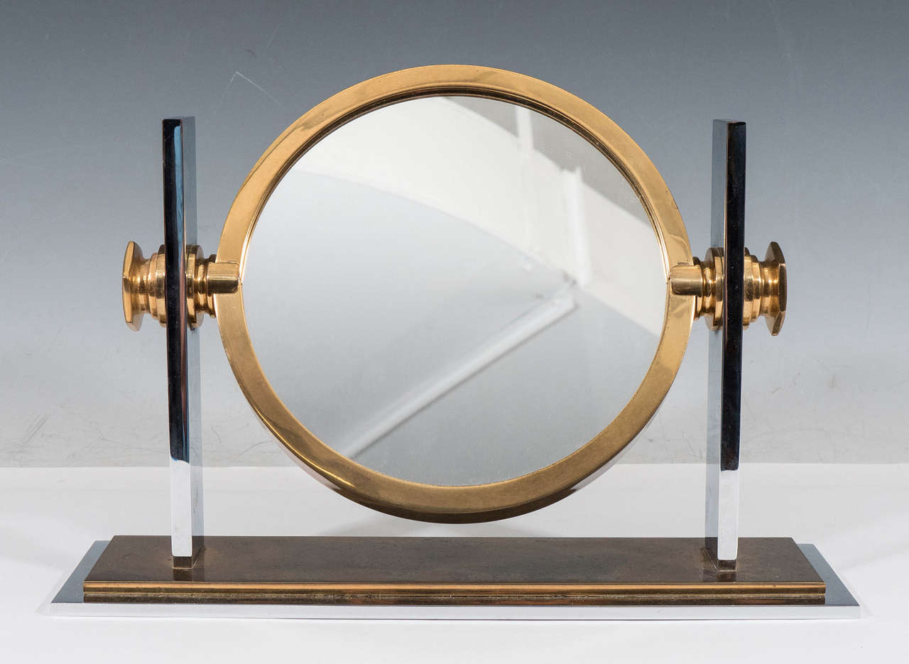 A vintage vanity mirror, produced circa 1970s by designer Karl Springer, inset in a Classic brass frame, with chrome supports, above a rectangular brass and chrome base. Good vintage condition with some age appropriate wear and minimal pitting to