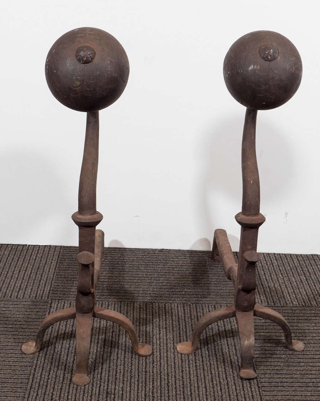 A unique pair of early 19th century antique andirons, possibly American in origin, in cast iron, surface etched with stylistic details, with ball-form heads above 'gooseneck' stems, on arched legs and penny feet. Good vintage condition with age