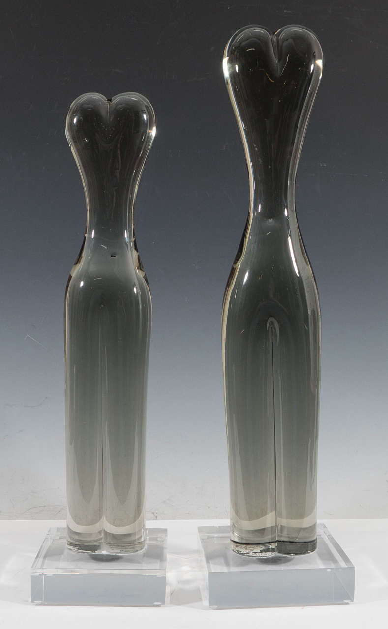 A pair of highly unique, studio glass sculptures, in the form of short and tall abstracted female torsos on Lucite bases. Markings included, artist's signature and date are illegible, with serial number [13/100], etched to the bottom of both