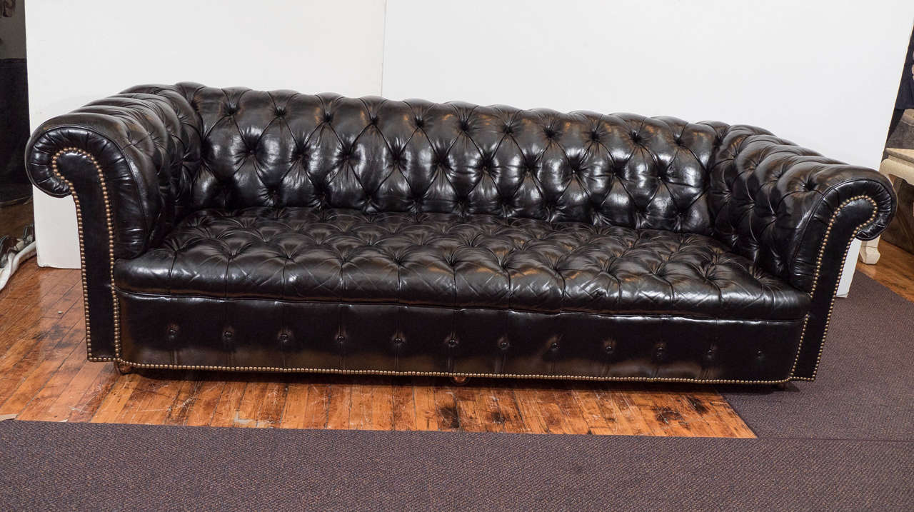 A vintage Chesterfield sofa, possibly English in origin, upholstered in black leather, with button tufting and brass nailhead beading. Good vintage condition, with a few nailheads missing, and a bit of cracking to the leather, consistent with age