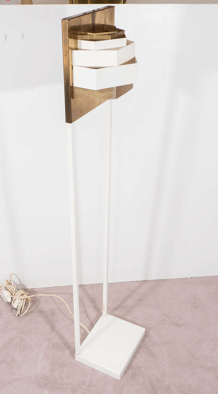 A vintage sculptural floor lamp, possibly German in origin, with a three-tiered, layered, white enamel shade, affixed to a perforated back plate in brass, on white enamel Dual pole legs and square base. Original European wiring and socket, requires