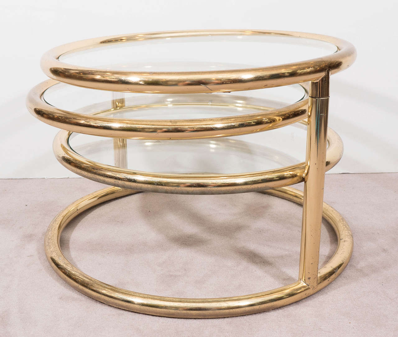 A vintage coffee table, produced, circa 1970s in the style of Milo Baughman, with three-tiered circular polished brass frames, inset with glass tops, above a ring shaped base, two of the table surfaces swivel and extend outwards, the lowest is set
