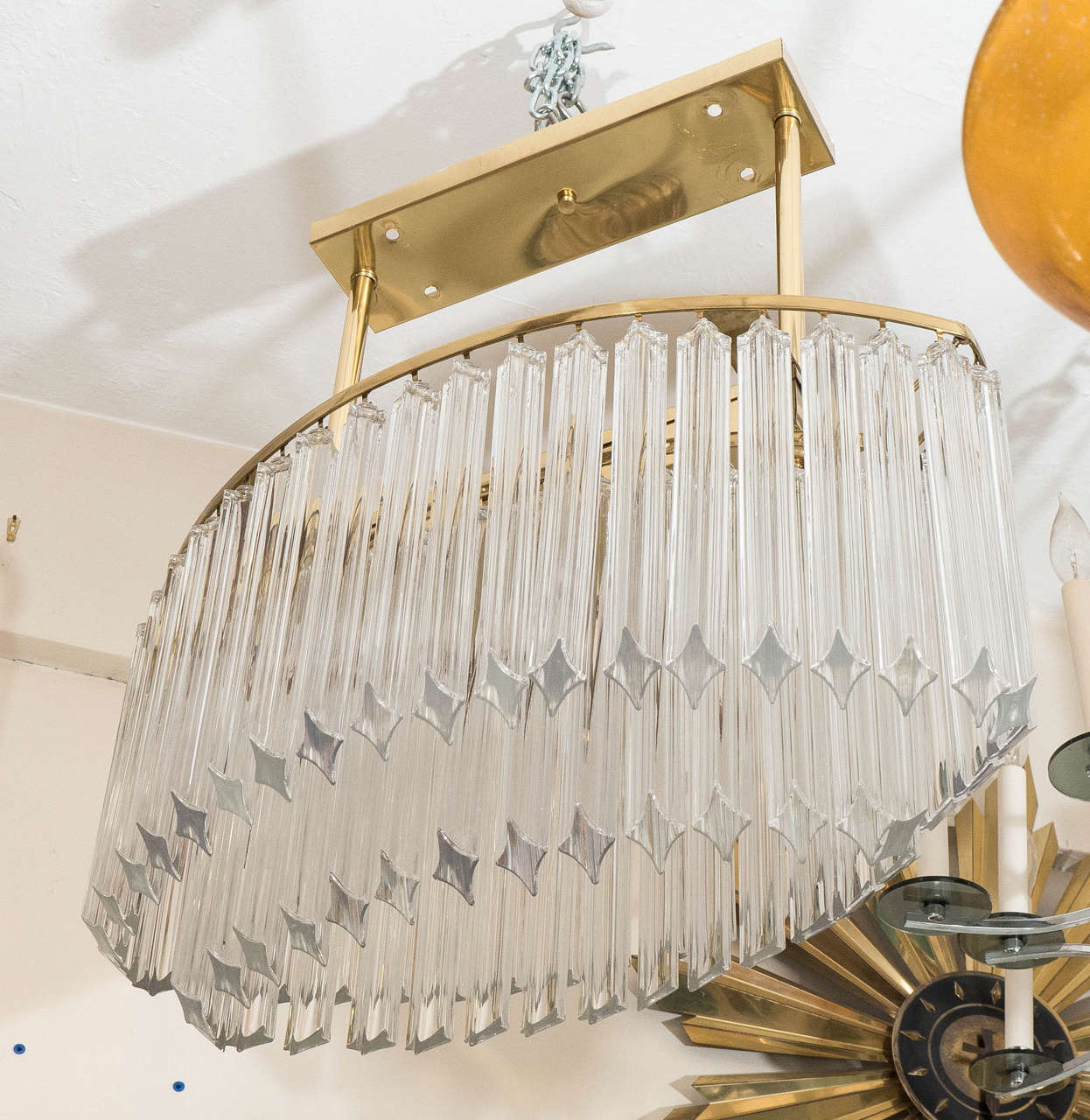 A vintage two-tiered chandelier, produced by Venini circa 1970's, with an oval shaped polished brass ring, affixed by two rods to a rectangular ceiling plate, decorated with rows of triedi glass prisms. Wiring and sockets to US standard, requires