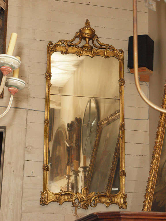 A French 2 glass plate mirror in a giltwood frame. A carved urn with flame at the crown with fluted sides with intricate foliate carvings.