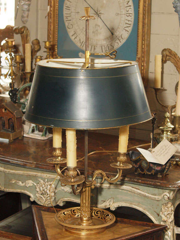 A gilt bronze bouillotte lamp with an adjustable green tole shade. A fluted column in a circular pierce plate supports the 3 electrified arms.