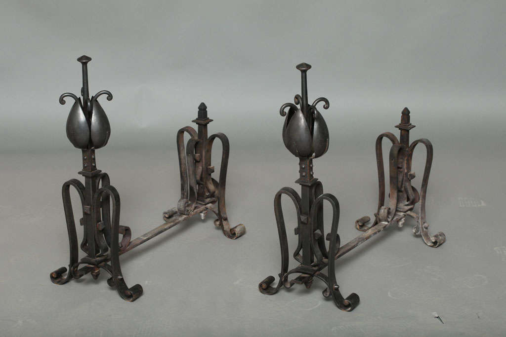 A rare and unusual pair of English Arts & Crafts blackened steel andirons with stylized tulip finials and ornate overscale log supports.