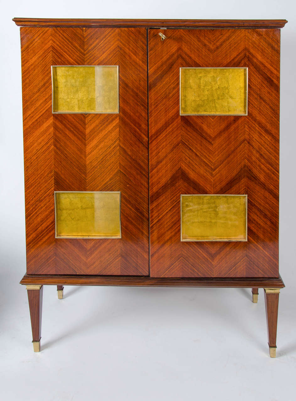 Neoclassical mid-1940's bar cabinet by mid-century Milanese architect Paolo Buffa .The bar is created from walnut veneer and features spectacular herringbone illuminated prominent doors which are recessed with four gold leaves panels. The doors open