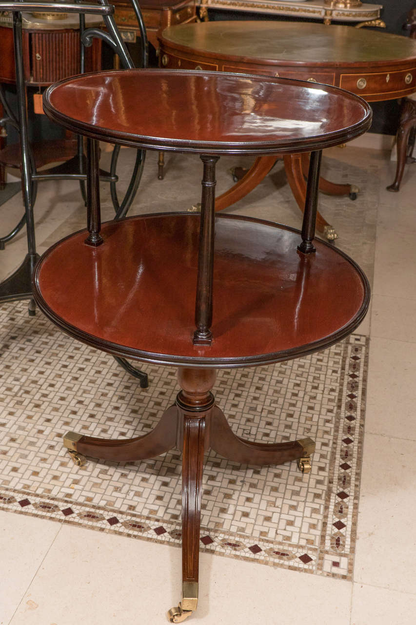 A rare pair of Regency mahogany two-tier dumbwaiters with pedestal bases, sabre legs and brass casters.
